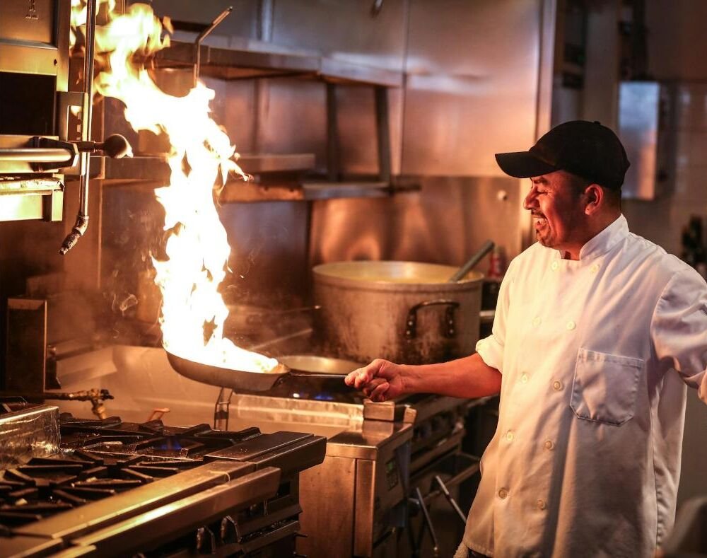 A chef cooking over a flaming pan in a restaurant kitchen