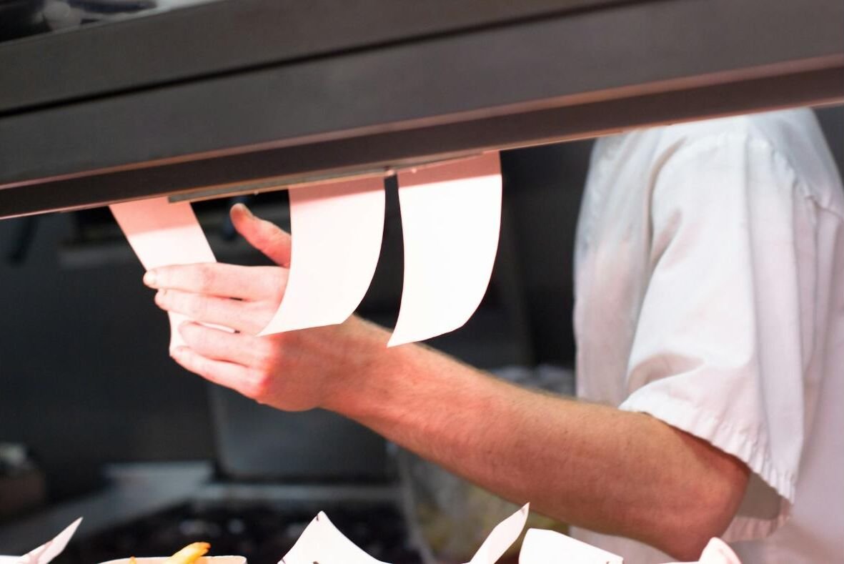 A kitchen worker pulling printed order tickets from a rail